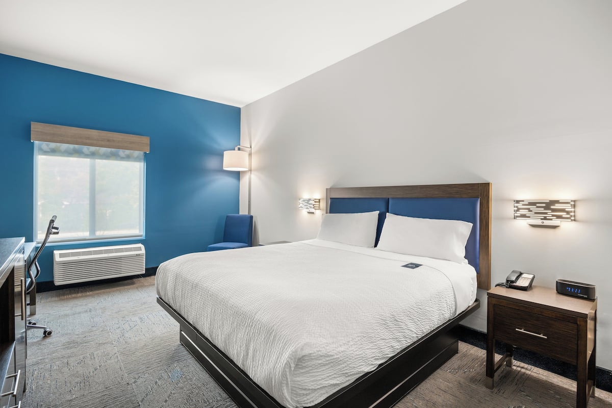 Una habitación de hotel con cama, mesita de noche, lámpara y ventana con persianas.