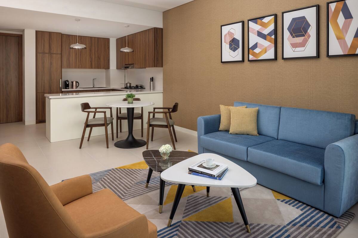 Un salon moderne avec un canapé bleu, une table basse et un coin repas, la cuisine étant visible au fond.