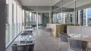 Un espace de restauration moderne avec des murs en verre, des tables blanches et des chaises grises.