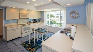 A compact kitchen with white cabinets, a microwave, a stove, and a sink. There is a window providing natural light and a view of the outside. - 646 New Haven Ct (Fripp Island)