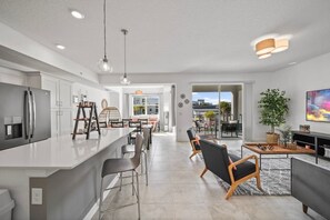 Une cuisine moderne dotée d’un îlot central, d’un coin repas avec des chaises et d’un salon avec un canapé et une télévision.