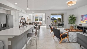 A modern kitchen with a central island, dining area with chairs, and a living room with a sofa and TV. - 3180-207 Resort Pool View Disney Universal Orlando (Kissimmee)