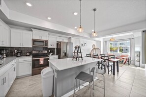 Une cuisine moderne avec des meubles blancs, des appareils en acier inoxydable et un îlot central doté de tabourets de bar.