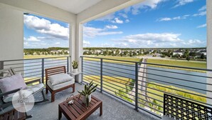 A balcony with a view of a residential area, a wooden bench, a small table with a plant, and a railing.
