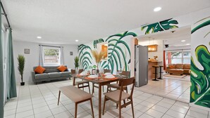 Ein modernes Wohnzimmer mit Essbereich, ausgestattet mit einer Couch, einem Esstisch für vier Personen und einem großen Fenster.