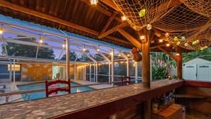 Ein Außenbereich mit Bar, Pool, Holzterrasse und Lichterketten.