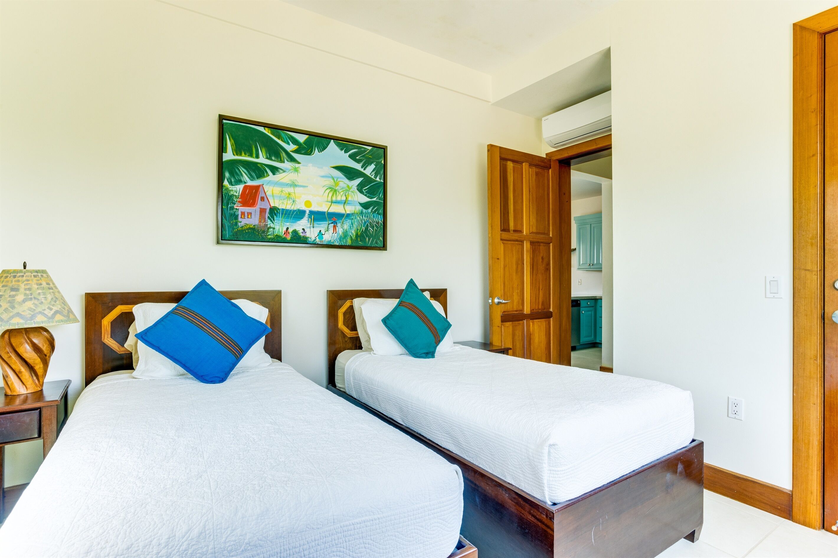 A hotel room with two beds, a painting on the wall, and a wooden door.