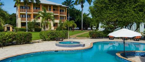 A hotel with a swimming pool, palm trees, and a well-maintained garden.