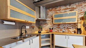 A kitchen with a brick wall, wooden cabinets, a stainless steel sink, and a coffee maker. - Chic Artist Flat on Fun Brewery & Restaurant Strip (Philadelphia)