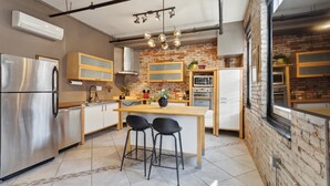 A modern kitchen with a central island, stainless steel appliances, and a brick accent wall. - Chic Artist Flat on Fun Brewery & Restaurant Strip (Philadelphia)
