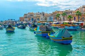 A marina with colorful boats docked, a waterfront promenade, and buildings in the background.