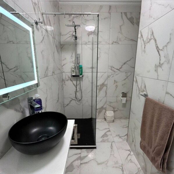 A bathroom with a black vessel sink, a glass-enclosed shower, marble tiles, a towel rack, and a mirror.