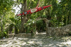A red kayak tied to a tree, a stone wall, and a welcome sign in a lush, green environment. - Yayum Bacalar (Bacalar)