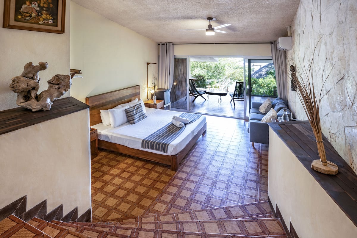 Habitación de hotel con cama, sofá, mesa de comedor y vistas al exterior.