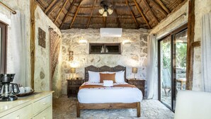 A stone-walled bedroom with a wooden bed, a ceiling fan, and a window overlooking a garden. - Yayum Bacalar (Bacalar)