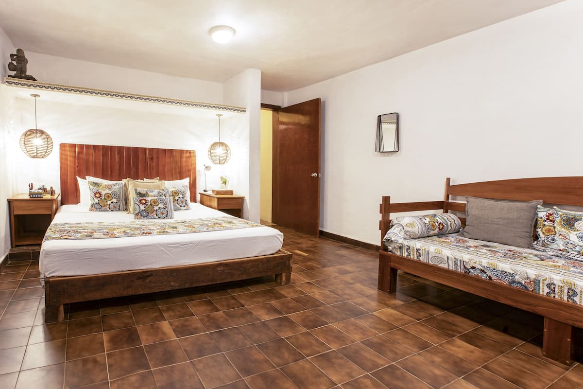 Un dormitorio con una cama grande, una cama más pequeña, suelo de madera y cabecero de madera.