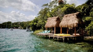 A tropical beach with thatched-roof huts, clear blue water, and boats in the distance. - Yayum Bacalar (Bacalar)