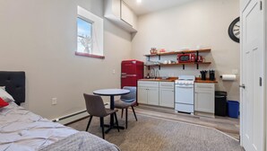 A compact room with a bed, a small dining table with chairs, a kitchenette with a microwave, stove, and refrigerator, and a window with a view.