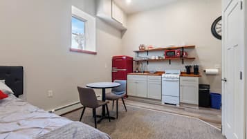 Een knus verblijf met een bed, een eettafel met stoelen, een kitchenette met een magnetron, fornuis en koelkast, en een raam met uitzicht.
