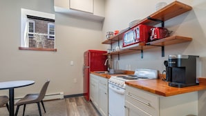 A compact kitchen with a red refrigerator, white stove, and wooden shelves above the counter.