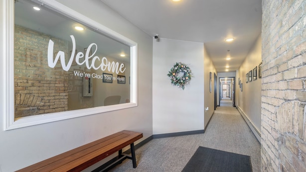 A hallway with a welcome sign, a bench, a wreath, and a brick wall.
