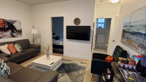 A modern living room with a sofa, coffee table, and artwork. There is a TV mounted on the wall and a painting on the adjacent wall.