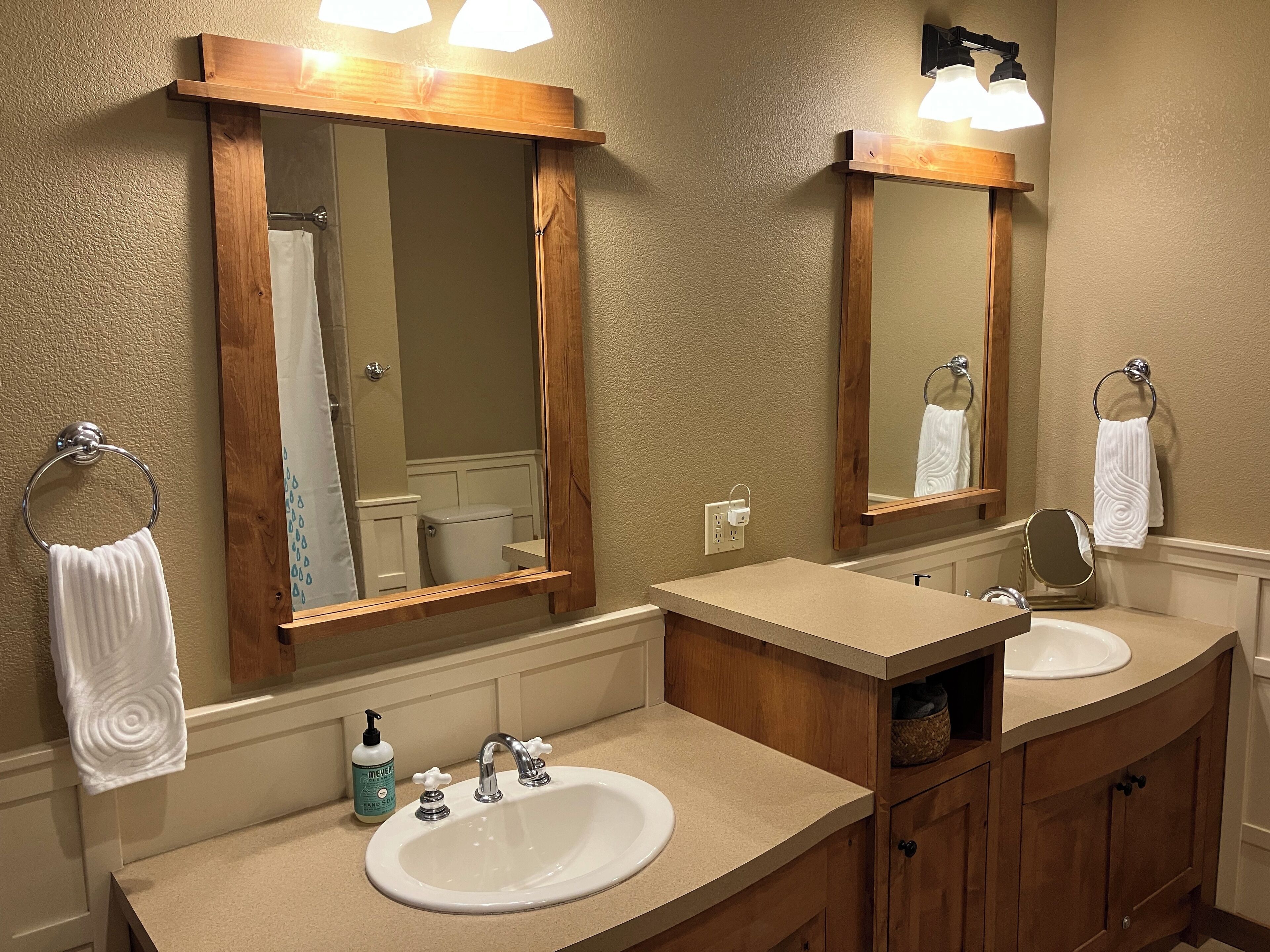 A bathroom with two sinks, a mirror, a towel rack, and a shower visible in the mirror.