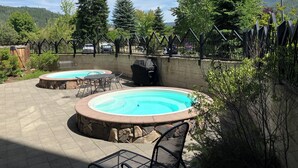 Un patio trasero con dos jacuzzis, una parrilla y un área de estar con sillas y una mesa.