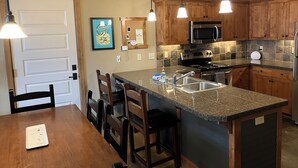 Una cocina con gabinetes de madera, encimera de granito, electrodomésticos de acero inoxidable e iluminación colgante.