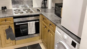 Une cuisine compacte dotée de meubles en bois, d’une cuisinière en acier inoxydable, d’un four encastré, d’un four à micro-ondes et d’un lave-linge à chargement frontal.
