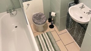 Une salle de bain avec une baignoire, des toilettes, un lavabo et une petite plante en pot posée sur le comptoir.