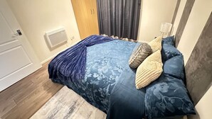 Une chambre à coucher avec un lit, une armoire en bois, une fenêtre avec des rideaux et une table de chevet avec une lampe.