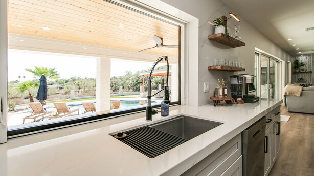 A modern kitchen with a large window, a built-in sink, and wooden ceiling panels.