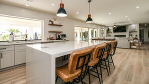 A modern kitchen with a large island, bar stools, pendant lighting, and a view of the outdoors.