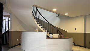 Un interior moderno con un mostrador de recepción curvo, una escalera de caracol y un ventanal que proporciona luz natural.