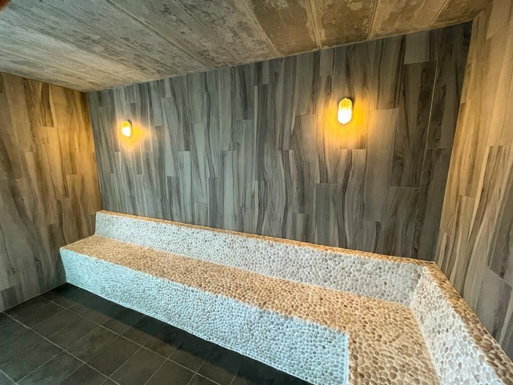 Eine Bank mit strukturierter Oberfläche, vor einer Wand mit Holzpaneelen und zwei Wandleuchten.