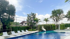 A swimming pool with lounge chairs, surrounded by greenery and a clear sky.