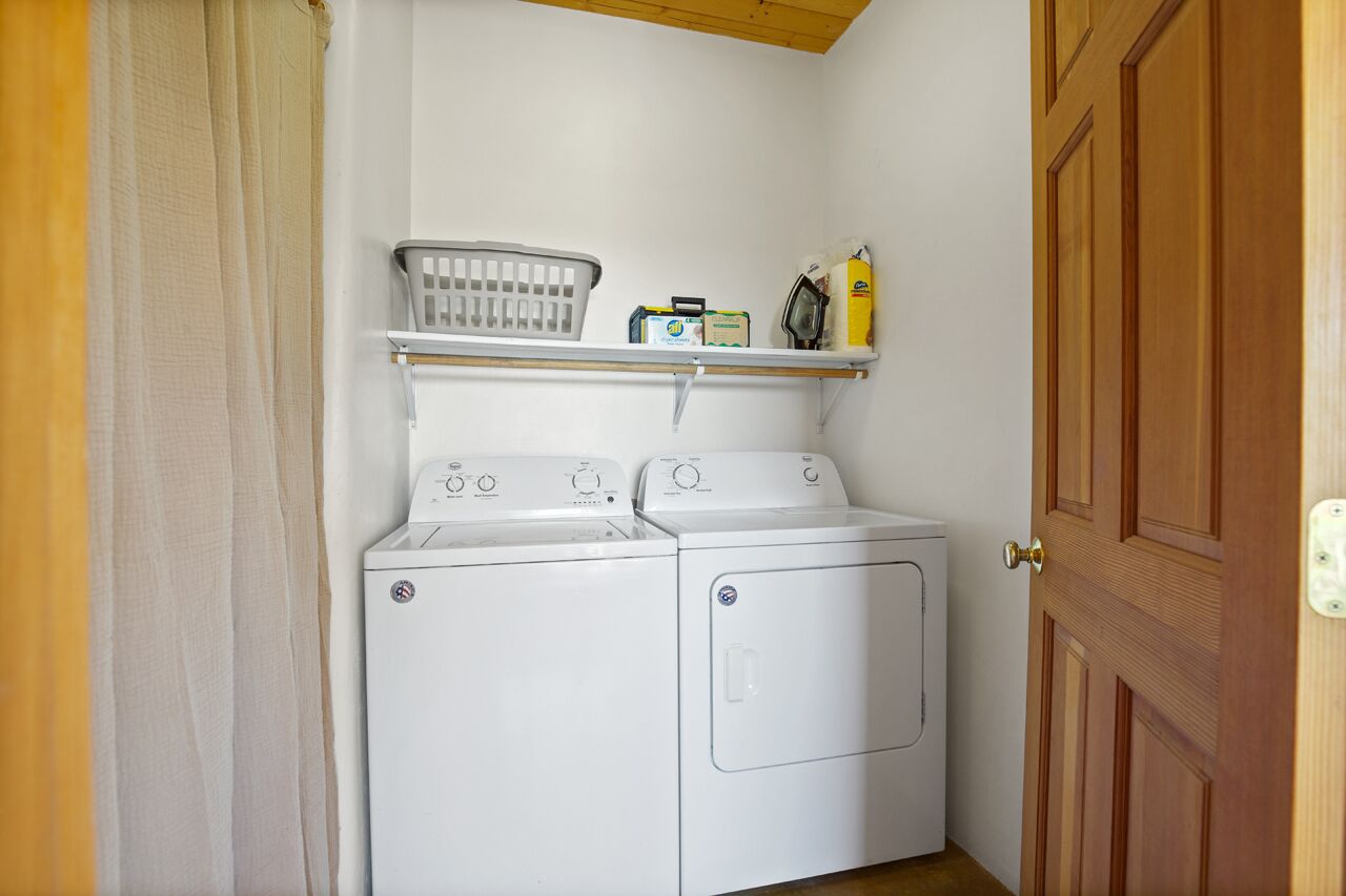A laundry room with a washing machine and dryer, a shelf with laundry supplies, and a wooden door.