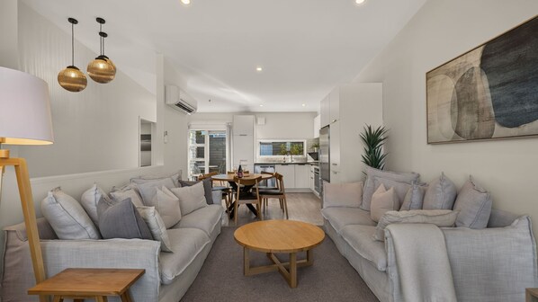 A modern living room with two sofas, a coffee table, and a dining area with a table and chairs. - Remarkable Woodsider - family friendly walk to town (Queenstown)