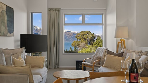 A hotel room with a large window offering a scenic view of mountains and trees. There is a TV, a lamp, and a table with wine glasses. - Remarkable Woodsider - family friendly walk to town (Queenstown)