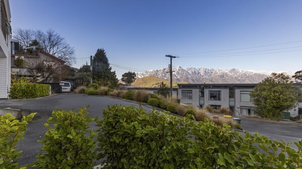 A residential street with a modern building, a parked van, and a mountain range in the background. - Remarkable Woodsider - family friendly walk to town (Queenstown)