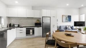 Une cuisine moderne avec des meubles blancs, un réfrigérateur en acier inoxydable et un coin repas comprenant une table et des chaises en bois.