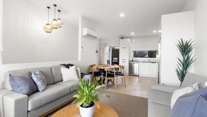 Un salon moderne avec un canapé gris, une table basse agrémentée d’une plante, et un coin repas avec une table et des chaises en bois.
