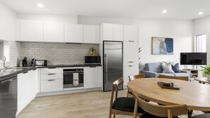 A modern kitchen with white cabinets, a stainless steel refrigerator, and a dining area with a wooden table and chairs. - Remarkable Woodsider - family friendly walk to town (Queenstown)