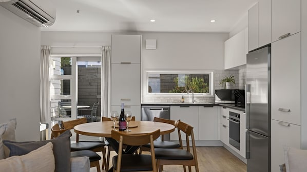 A modern kitchen with white cabinets, a stainless steel refrigerator, and a dining area with a round table and chairs. - Remarkable Woodsider - family friendly walk to town (Queenstown)