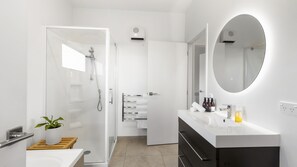 A modern bathroom with a glass shower enclosure, a white vanity with a mirror, and a potted plant.