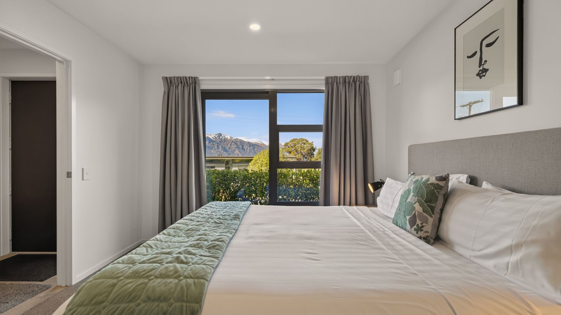 Une chambre avec un grand lit, une vue sur les montagnes par la fenêtre et une porte donnant sur une autre pièce.