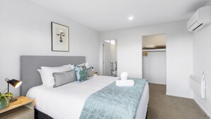 A modern bedroom with a bed, bedside table, lamp, and a framed picture on the wall. - Remarkable Woodsider - family friendly walk to town (Queenstown)