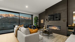 A modern living room with a large window, a fireplace, and a flat-screen TV mounted on the wall. - Highview Hideaway -  stunning lake and mountain views. (Queenstown)