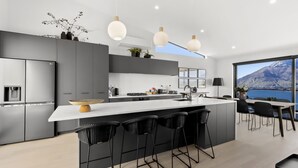 A modern kitchen with a large island, bar stools, a refrigerator, and a view of a mountain. - Highview Hideaway -  stunning lake and mountain views. (Queenstown)